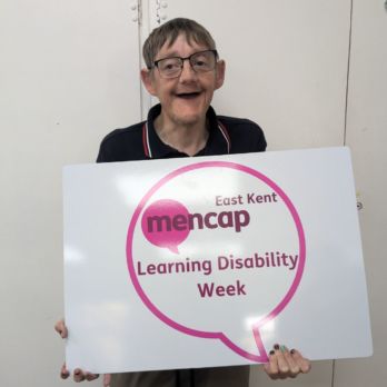 Man smiling holding a Learning Disability Week sign