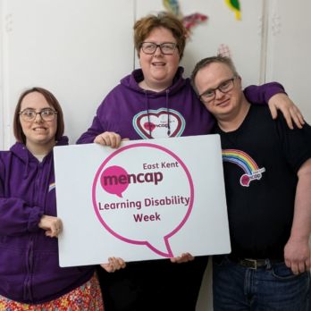 Two women and one man smiling holding a Learning Disability Week sign