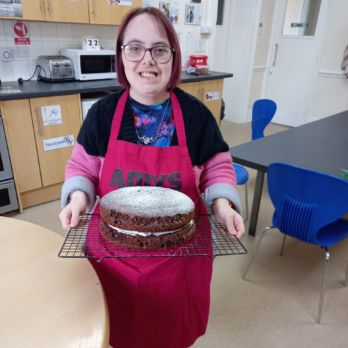 Amy holding a chocolate cake on a baking tray