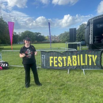 Lady smiling with her thumbs up in a park next to a Festability sign