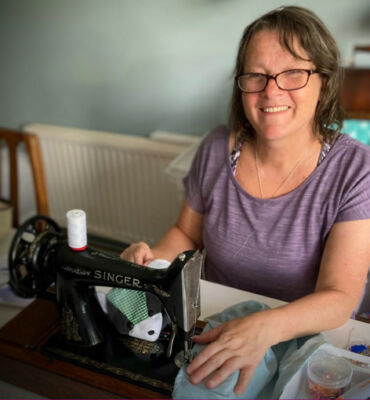 Lady wearing glasses and purple top smiling next to her sewing machine