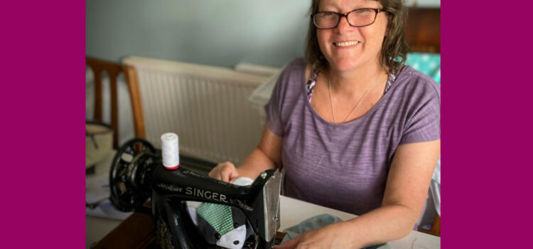 Lady wearing glasses and purple top smiling next to her sewing machine