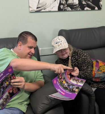 Man and woman on sofa reading the autumn newsletter. The man is pointing to something in the newsletter.