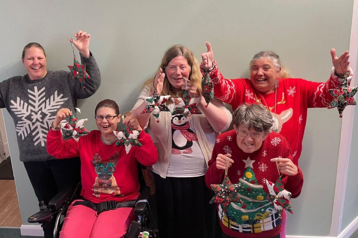 Five smiling ladies wearing festive jumpers and holding stars