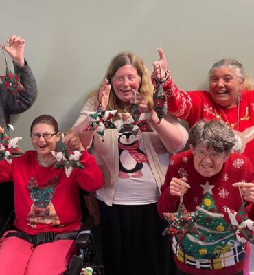 Five smiling ladies wearing festive jumpers and holding stars