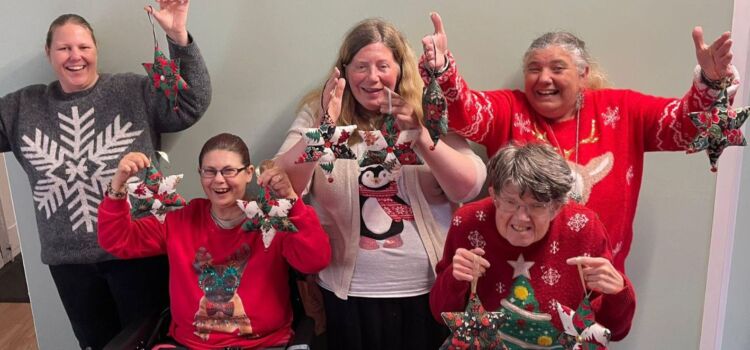 Five smiling ladies wearing festive jumpers and holding stars